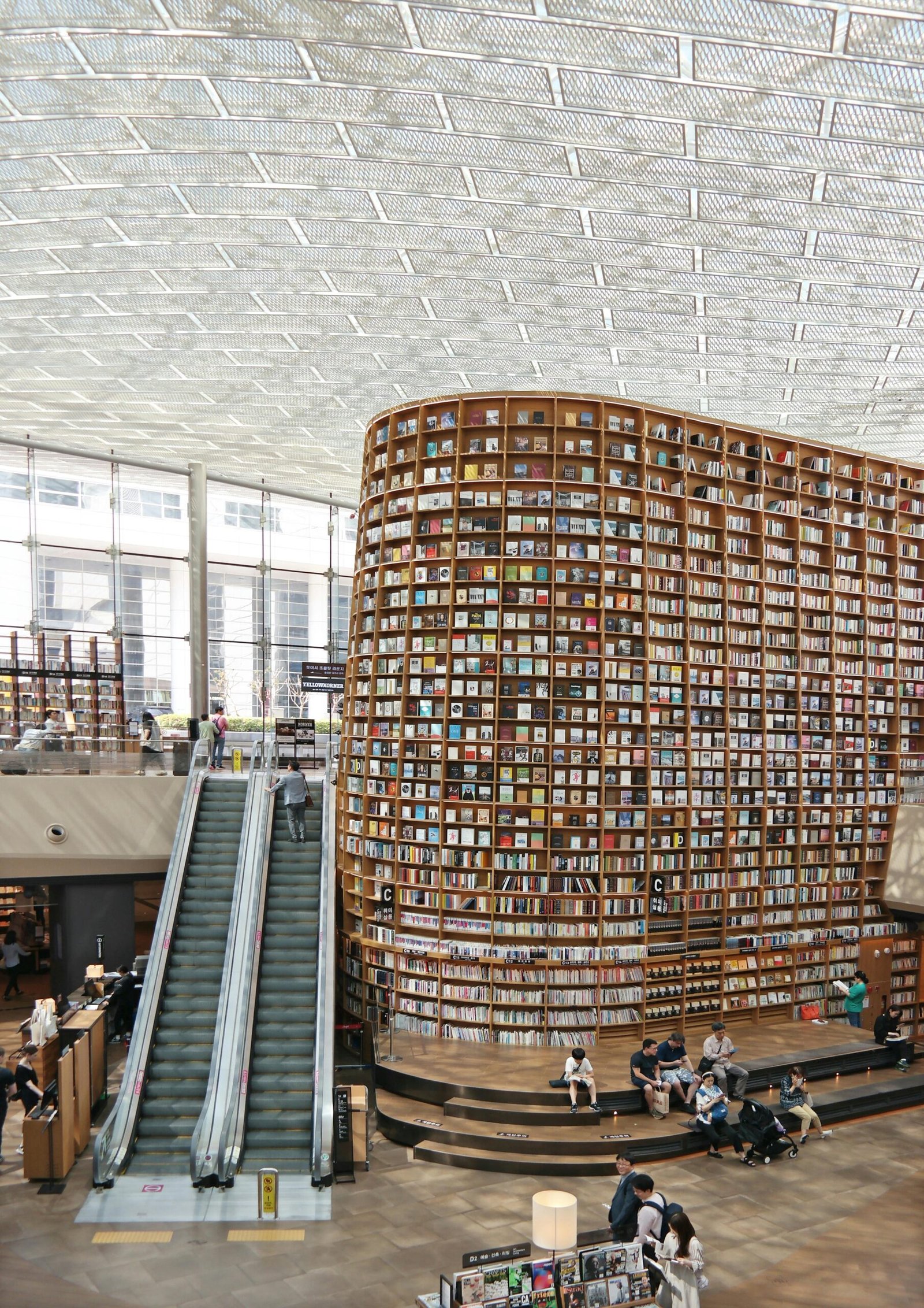 Interior view of a modern library in Seoul with a vast bookshelf and escalators under a glass ceiling.